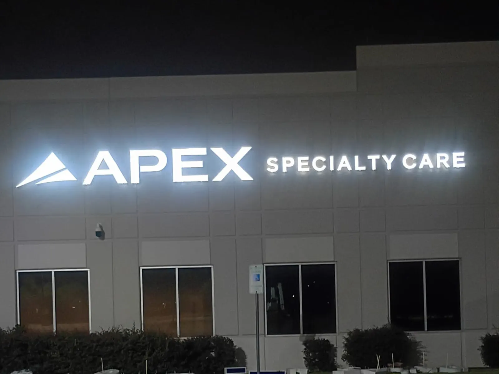Apex Specialty Care white channel letters and logo lit at night on a two-story building