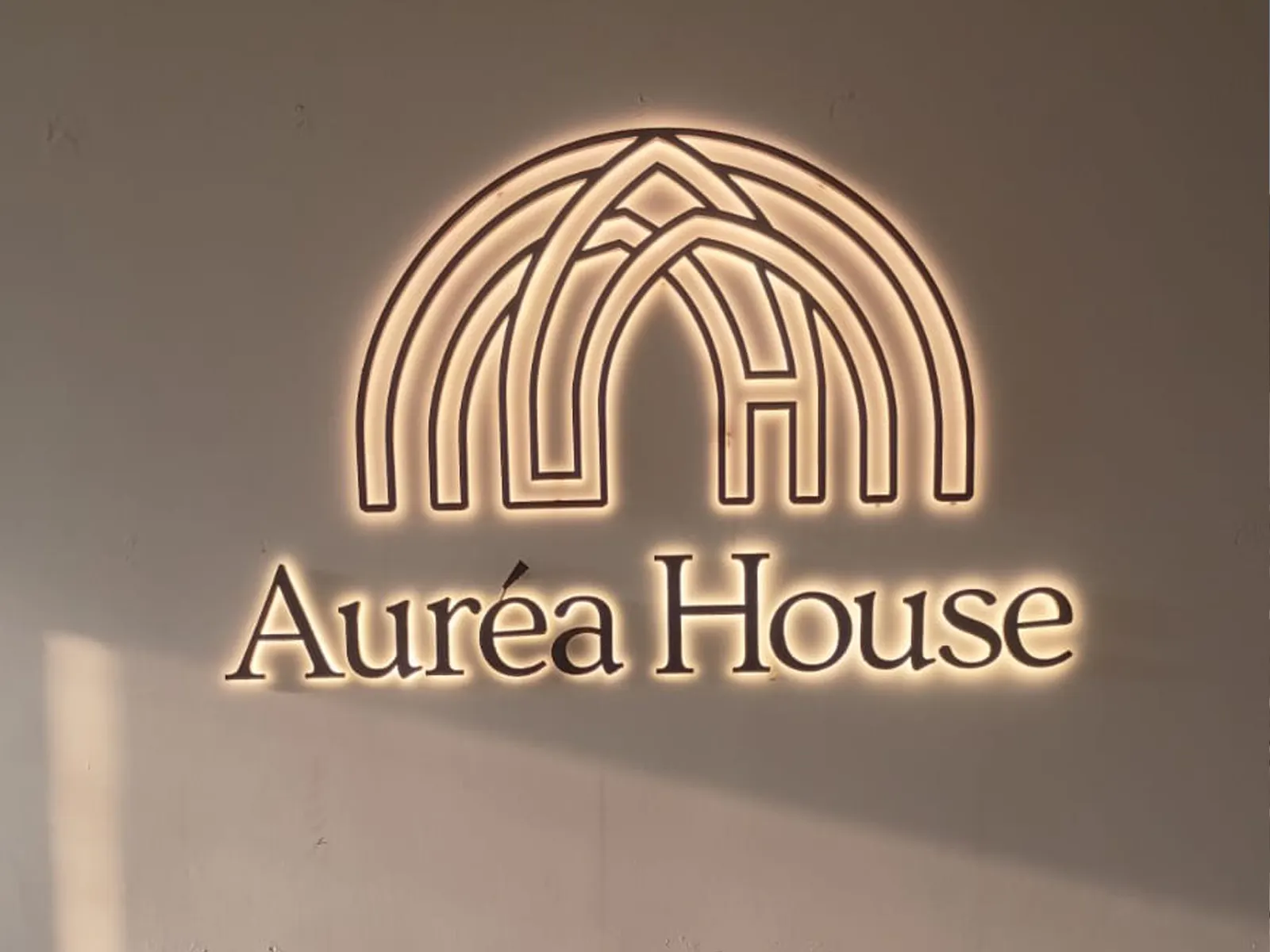Aurea House halo-lit arch logo and letters glowing on a light interior wall