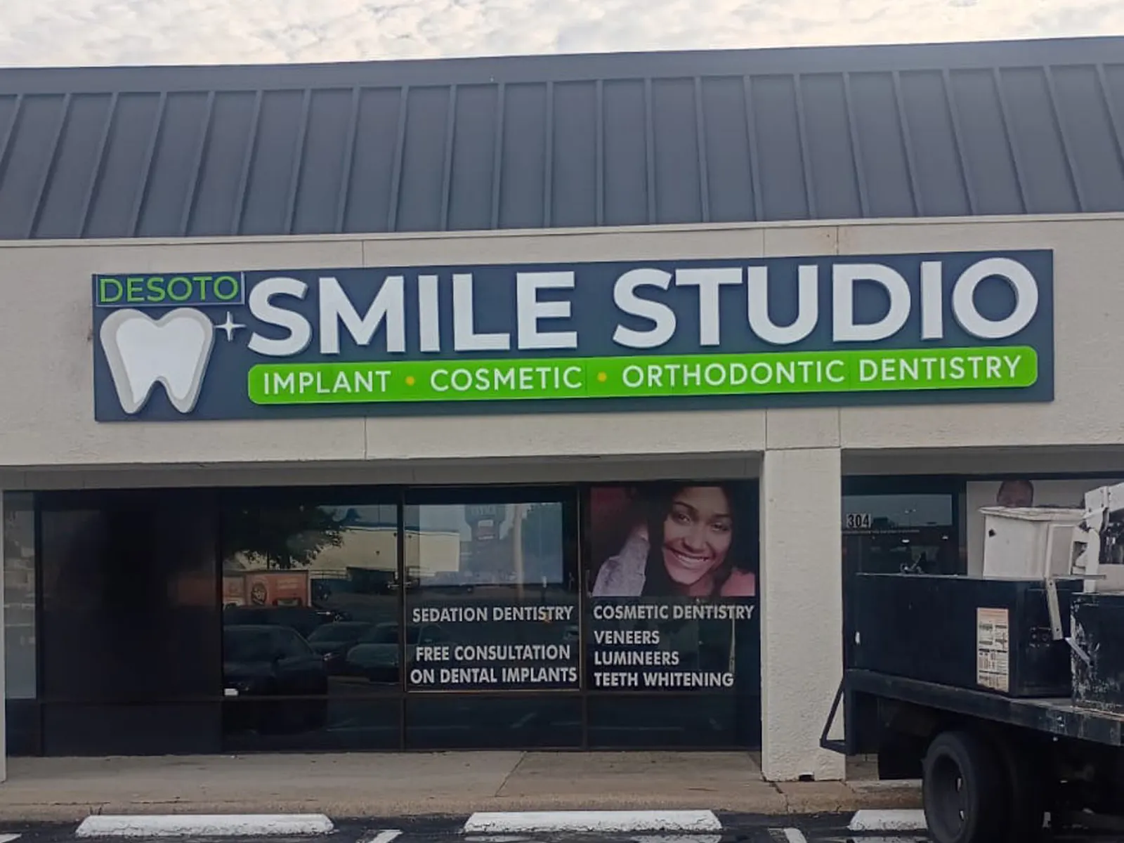 DeSoto Smile Studio lit cabinet sign with a tooth logo above a dental office, a service truck at right