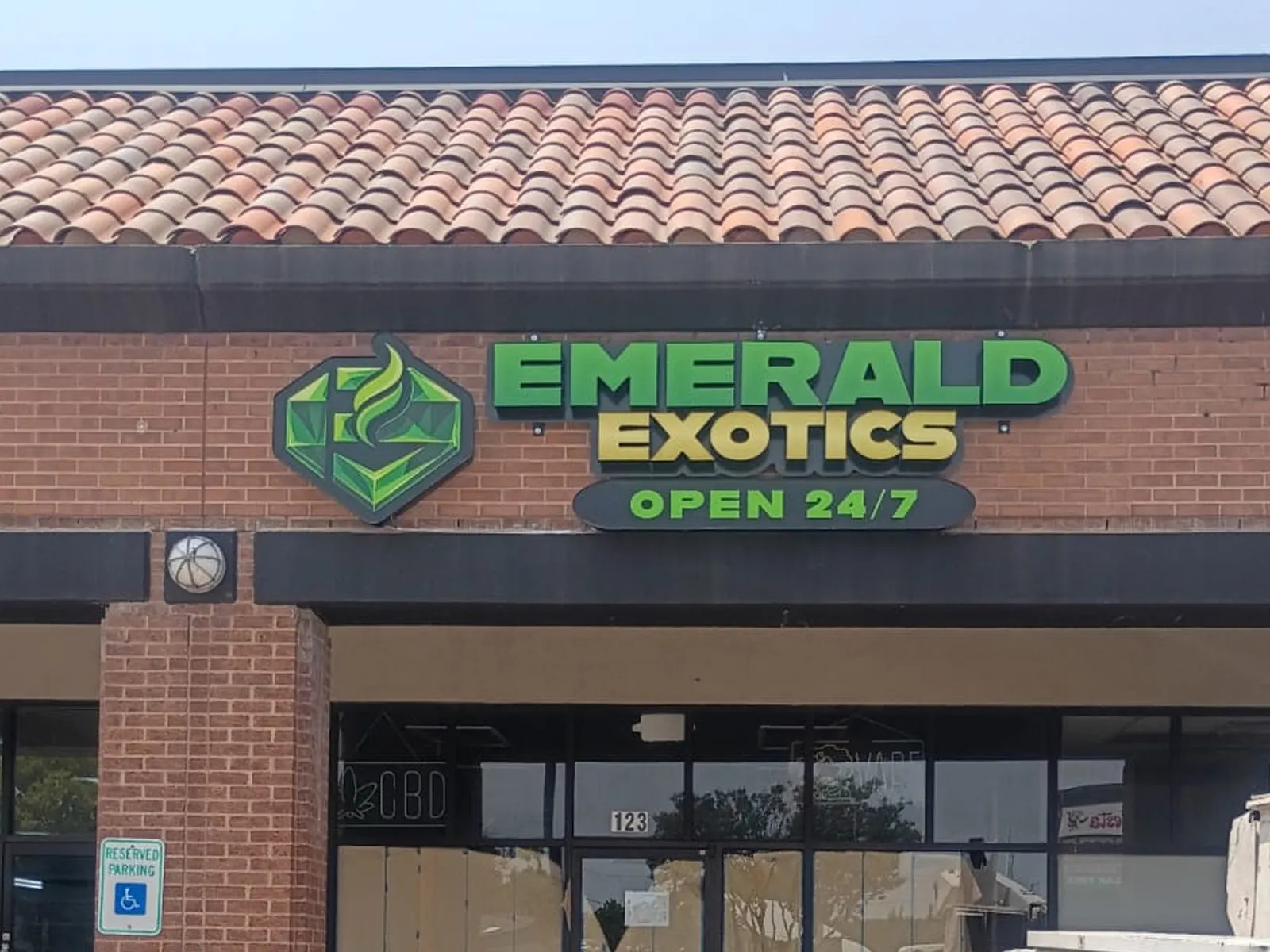 Emerald Exotics green channel letters and logo with an Open 24/7 line above a brick storefront