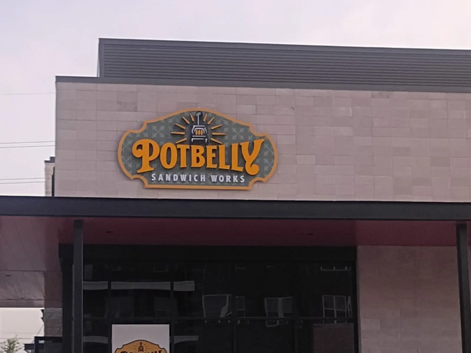 Potbelly Sandwich Works logo sign on a restaurant facade at sunset