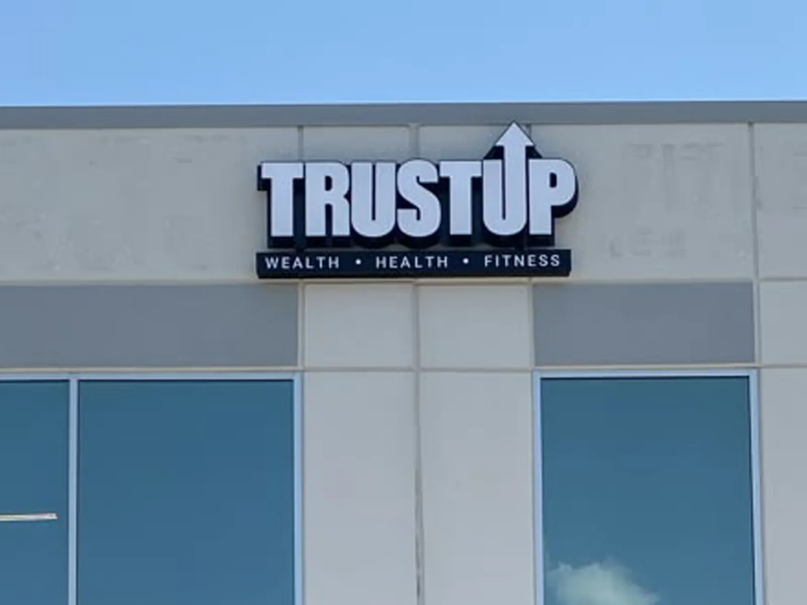 TrustUp channel letters with an arrow and a Wealth, Health, Fitness line on a white facade