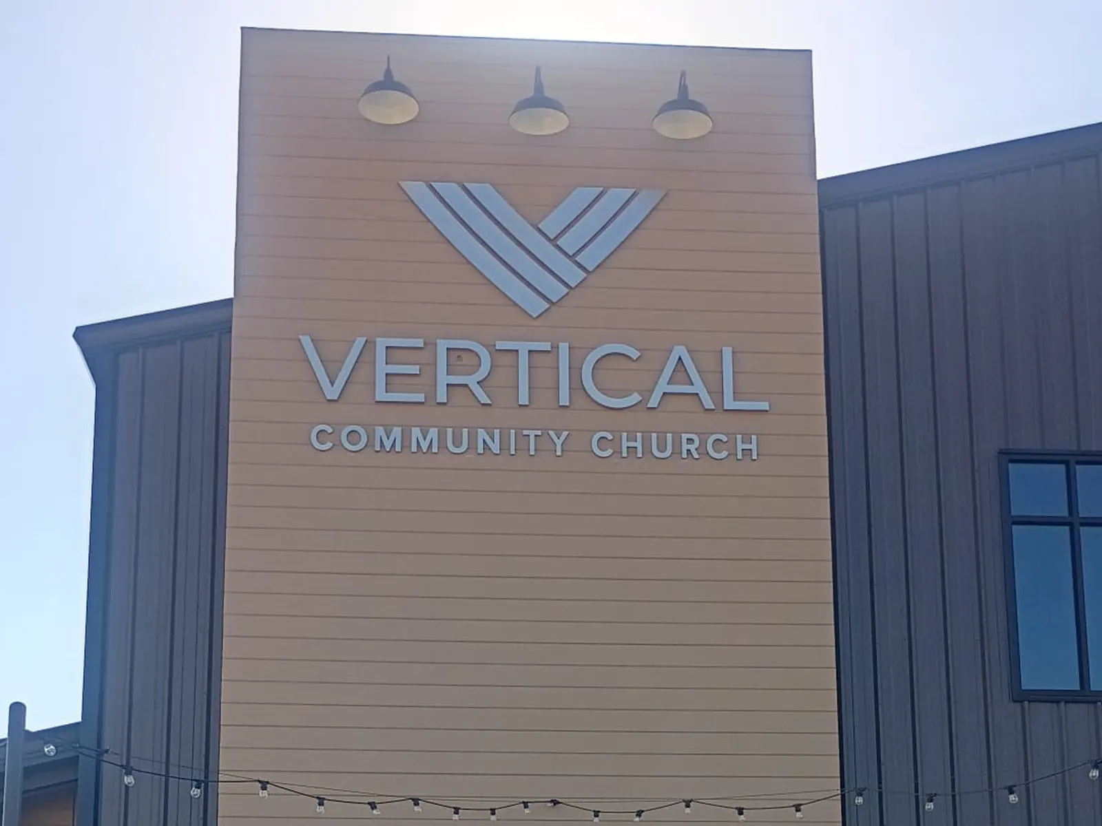 Vertical Community Church logo and letters on a tall wood-look facade with gooseneck lights